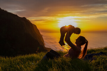 Wall Mural - Mother lifting up child on meadow with breathtaking sunset at viewing point Miradouro do Ponta da Ladeira, Madeira island, Portugal, Europe. Panoramic view of majestic coastline of Atlantic Ocean. Awe