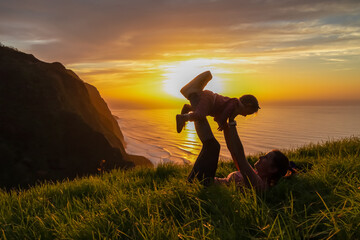 Wall Mural - Mother lifting up child on meadow with breathtaking sunset at viewing point Miradouro do Ponta da Ladeira, Madeira island, Portugal, Europe. Panoramic view of majestic coastline of Atlantic Ocean. Awe