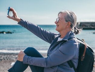 Sticker - Video call concept. Handsome smiling senior woman sitting outdoors face the sea talking on mobile phone using phone webcam to communicate in video chat