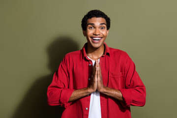 Wall Mural - Photo of cheerful excited man dressed red shirt arms together praying isolated green color background