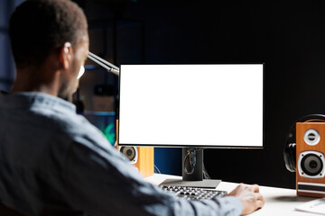 Man examines white display on workstation while telecommuting and uses empty screen on monitor. Male entrepreneur operates remotely from home with blank chromakey layout on his desk.