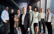 © CarlosBarquero - Business group portrait posing with confidence attitude. Successful diverse team looking at camera leading boss in front. Professional people workers in suits standing in office building corridor