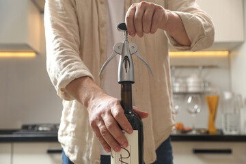 Wall Mural - Man opening wine bottle with corkscrew in kitchen, closeup