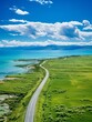 An aerial view of the vast expanse of Qinghai Lake with an endless sea and green grassland stretching to the horizon A white car is driving on the road leading towards the lake