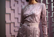 A woman model stand pose in silver and pink sequin maxi dress, closeup haft top light magenta dress long sleeve on a female model with decor studio wall