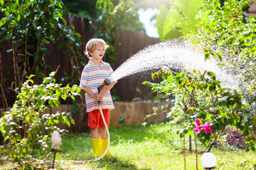 Boy watering flower in garden. Kid with water hose