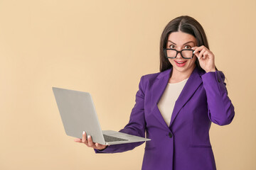 Surprised female programmer with laptop on beige background