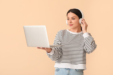 Female programmer in headphones with laptop on beige background