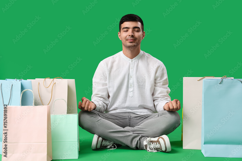 Handsome young man with shopping bags meditating on green background