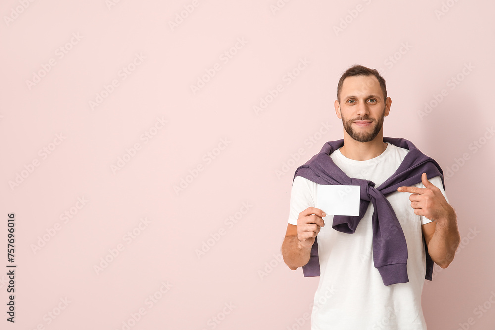 Young man pointing at blank ballot on pink background
