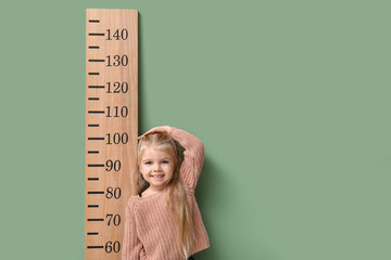 Wall Mural - Cute little girl measuring height on green background