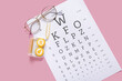 Stylish eyeglasses with eye test chart, tweezers and container for contact lenses on pink background