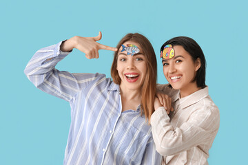 Wall Mural - Beautiful young happy women with paper fishes attached to their foreheads on blue background. April Fools Day celebration