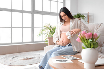 Wall Mural - Young pregnant woman with baby booties sitting on sofa at home