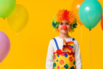 Poster - Funny little boy in clown costume with balloons on yellow background. April Fools Day celebration