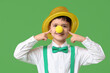 Funny little boy in clown nose with hat on green background. April Fools Day celebration