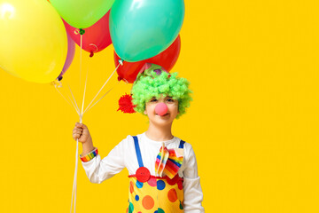 Poster - Funny little boy in clown costume holding balloons on yellow background. April Fools Day celebration