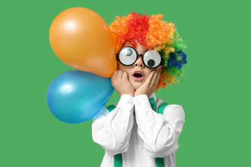 Poster - Surprised little boy in funny glasses and clown wig with balloons on green background. April Fools Day celebration