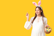 © Pixel-Shot - Young pregnant woman in bunny ears holding wicker basket with Easter eggs and beautiful roses on yellow background