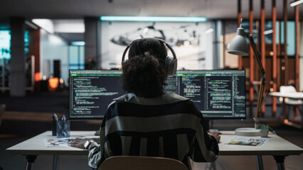 Wall Mural - Creative Office: Professional Black Female Programmer Uses Headphones, Working on Desktop Computer. Focused Coder, Software Engineer Developing App, Video Game. Listening to Podcast, Music. Back View.