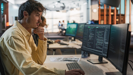 Wall Mural - Male Caucasian Game Programmer Coding On Desktop Computer In Game Design Studio Diverse Office. Focused Man Writes Lines Of Code, Does Gameplay Engineering For New Immersive 3D Survival Video Game.