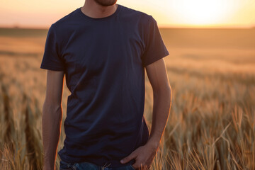Wall Mural - Caucasian male model wearing a navy blue crewneck blank mockup t-shirt with short sleeves in a field background at sunset , man face is not visible