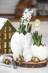 Wall Mural - Happy Easter. A spring hyacinth flower in an egg-shaped vase, Easter bunnies and eggs with a golden pattern on the table. There is a white kitchen in the background. Easter decor in the house.