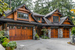 Stunning craftsman style home with a three car garage, elegant wooden doors, surrounded by vibrant spring landscaping.