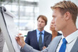 © Jeff Bergen/peopleimages.com - Businessman, flipchart and writing in office with meeting for project planning, stocks performance and profit management. Financial analyst, employee and person with presentation of data in workplace