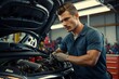 A man in a blue shirt and yellow gloves is working on a car engine. He looks focused and determined