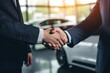 Close-up of a Professional Handshake at a Car Dealership, Signifying a Successful Business Agreement with Luxury Cars in Background