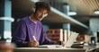 © Gorodenkoff - Portrait of a Smart Male Putting On Headphones and Working on a Laptop Computer. Young Man Doing a Homework Assignment and Preparing for Political Science Exams in a College Library