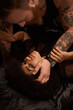 © LIGHTFIELD STUDIOS - bearded man with tattoos seducing young african american woman with curly hair on bed, desire
