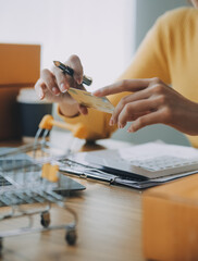 Wall Mural - Young woman holding a smartphone, tablet showing payment success and credit card with yellow parcel box as online shopping concept in office