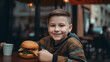 Cute fat happy boy 7 years old with a burger on cafe