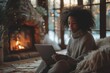 An ambient scene captures a woman relaxed in a warm sweater, using a laptop by a glowing fireplace