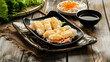Close-up of a plate with battered fish strips accompanied by soy sauce and vegetables on a wooden table
