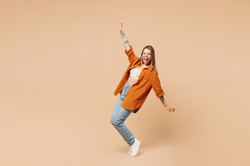 Poster - Full body young woman she wear orange shirt casual clothes stand on toes leaning back with outstretched hands dance isolated on plain pastel light beige background studio portrait. Lifestyle concept.