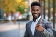 Young happy handsome smiling professional black businessman, happy confident positive male entrepreneur standing outdoor on street thumbs up
