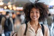 © Maelgoa - A black woman with a carefree smile, strolling through a bustling airport terminal with a rolling suitcase in tow