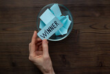 Fototapeta Mapy - Female hand holding lottery ticket with winner word near glass bowl full of paper sheets. Winner concept