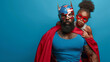 A joyful father wearing a helmet with an American flag design and red goggles gives a piggyback ride to his daughter, who wears a red superhero cape and goggles