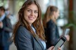 © romanets_v - A modern businesswoman is holding a tablet computer, smiling at the camera, with a colleague in the background.
