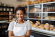 Shot of an attractive cheerful African American female baker smiling to the camera standing near the showcase in modern bakery
