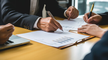 Poster - Close-up view of hands signing a document, with multiple individuals engaged in a business meeting around a table.