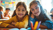 © MP Studio - Two young girls smiling and embracing each other in a classroom setting, with colored pencils and school supplies on the table in front of them.
