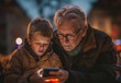 Young kid helps his grandpa surfing the web with his new mobile phone. Senior man learns internet and mobile phones. Dramatic light. Generation gap, family, affection between grandfather and grandson.