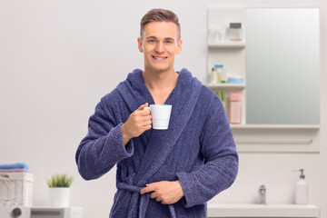 Wall Mural - Young man in a blue bathrobe holding a coffee mug and looking at the camera