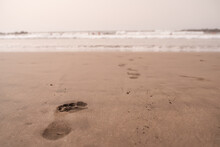A Sequence Of A Child's Footprints In The Sand Creates A Path Leading Towards The Ocean Waves In The Distance. Child's Footprints Leading To Ocean Waves.