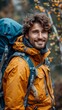 © TheGoldTiger - Smiling man with a beard wearing a yellow jacket, carrying a blue backpack, outdoors